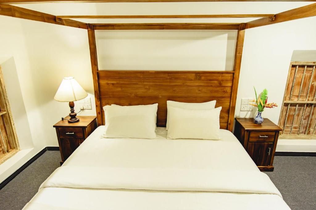 Ein Hotelzimmer mit einem hölzernen Kopfteil, einem Bett mit weißen Laken, einem Nachttisch mit einer Lampe und einer kleinen Pflanze auf dem Nachttisch.