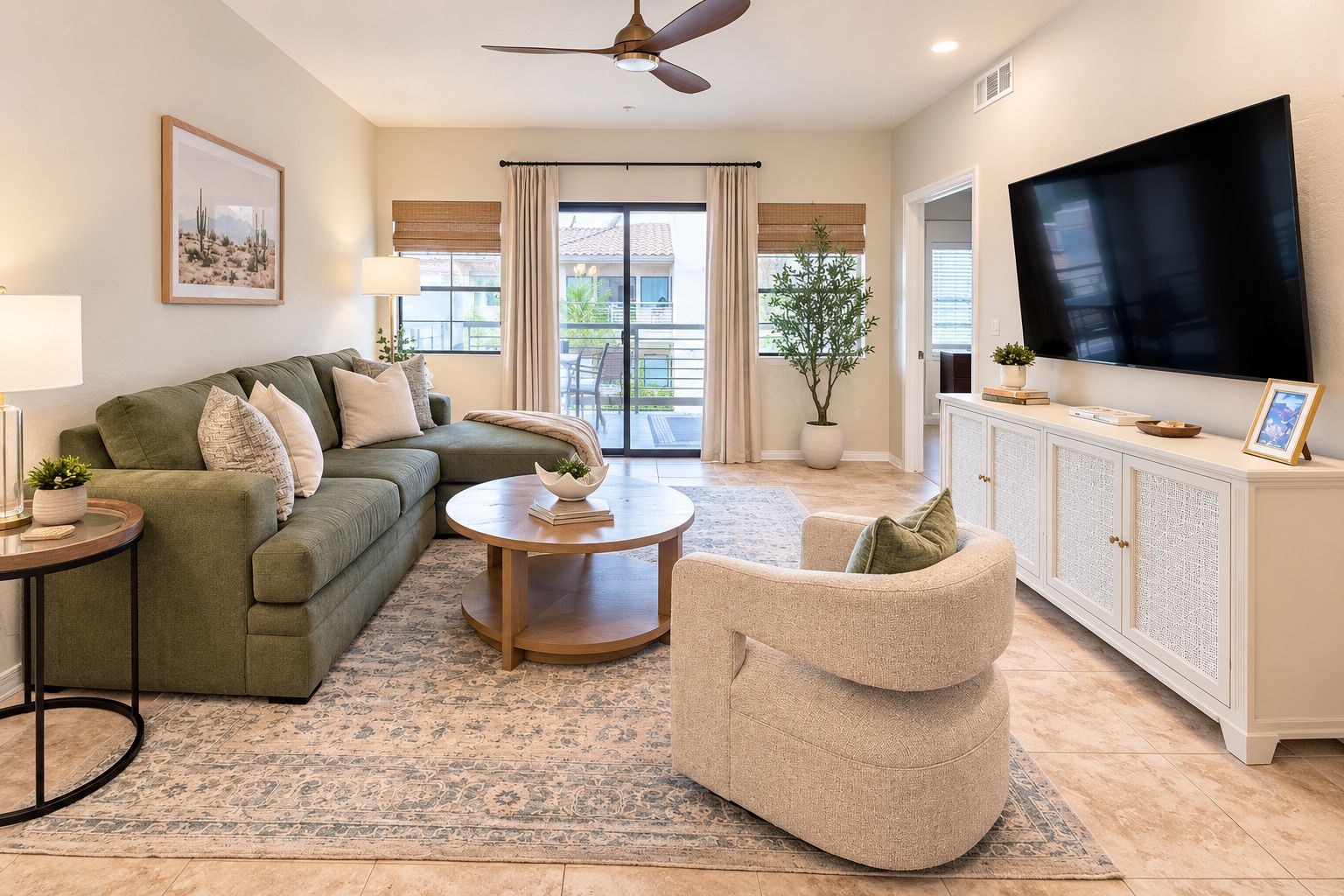 A living room with a green sofa, a round coffee table, a beige armchair, a flat-screen TV, and a white cabinet.
