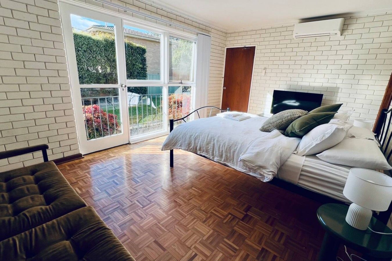 A bedroom with a bed, a bench, a bedside table, and a large window.