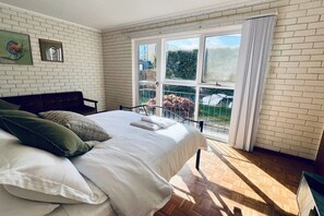 A bedroom with a large bed, a view of a garden through a sliding glass door, and a brick wall.