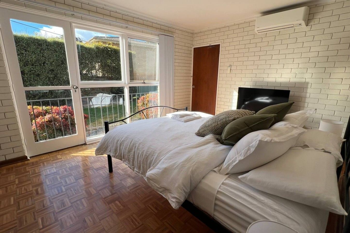 A bedroom with a bed, a TV, and a view of a garden through a glass door.