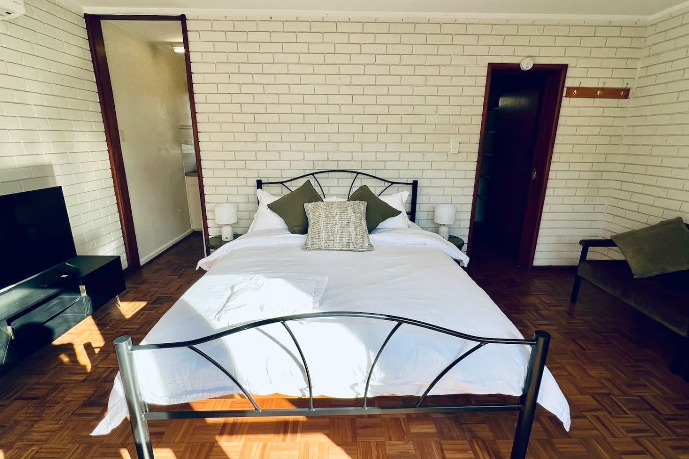 A room with a bed, a TV, a sofa, and a brick wall.