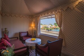 Quarto com teto estampado, janela com cortinas, sofá, mesa com uma tigela e luminária.