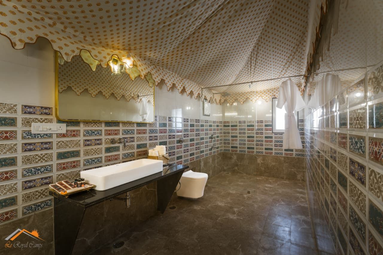 A bathroom with a large mirror, a sink, and a toilet. The walls are tiled with a patterned design.