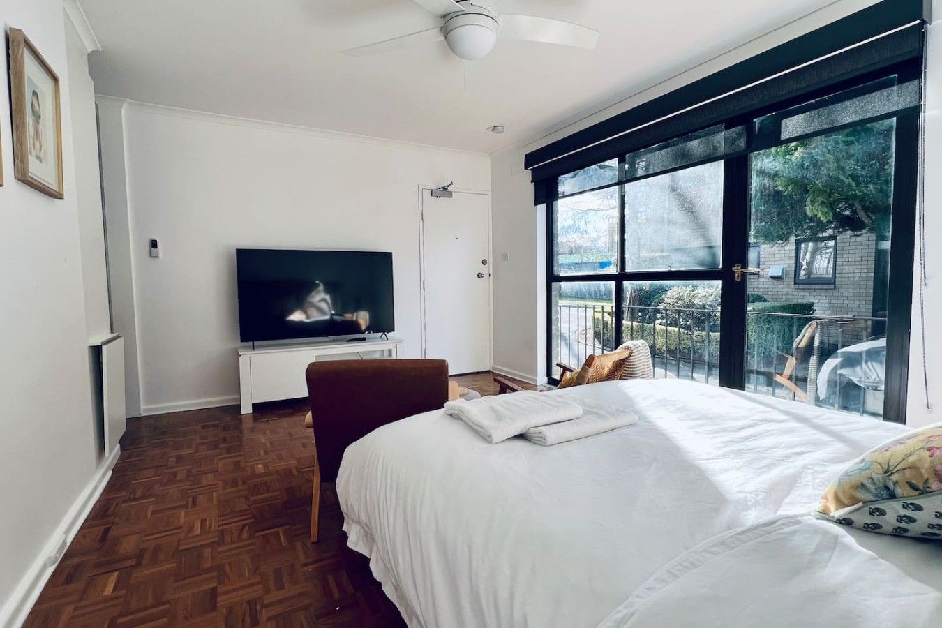 A bedroom with a bed, a television, a chair, and a window with a view of greenery.
