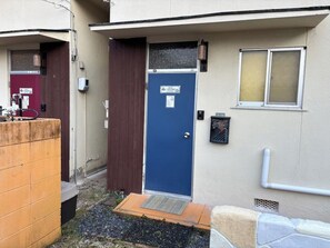 A blue door with a small window above it, a red door to the left, and a white pipe running along the wall. - New Listing (Hiroshima)