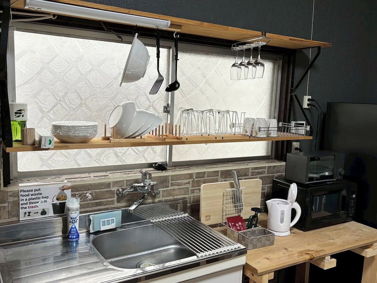 A kitchen with a sink, a microwave, and a coffee maker. There are utensils hanging above the sink and a sign instructing to put food waste in a plastic bag.
