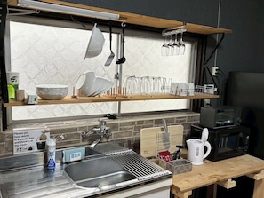 A kitchen with a sink, a microwave, and a coffee maker. There are utensils hanging above the sink and a sign instructing to put food waste in a plastic bag.