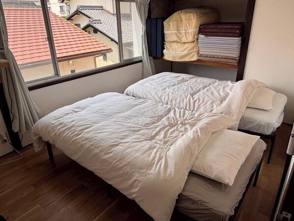 Une pièce avec un lit, une fenêtre avec des rideaux et une vue sur les bâtiments environnants.