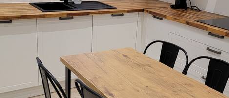 A compact kitchen with a wooden table and black chairs, a window with blinds, and white cabinets.