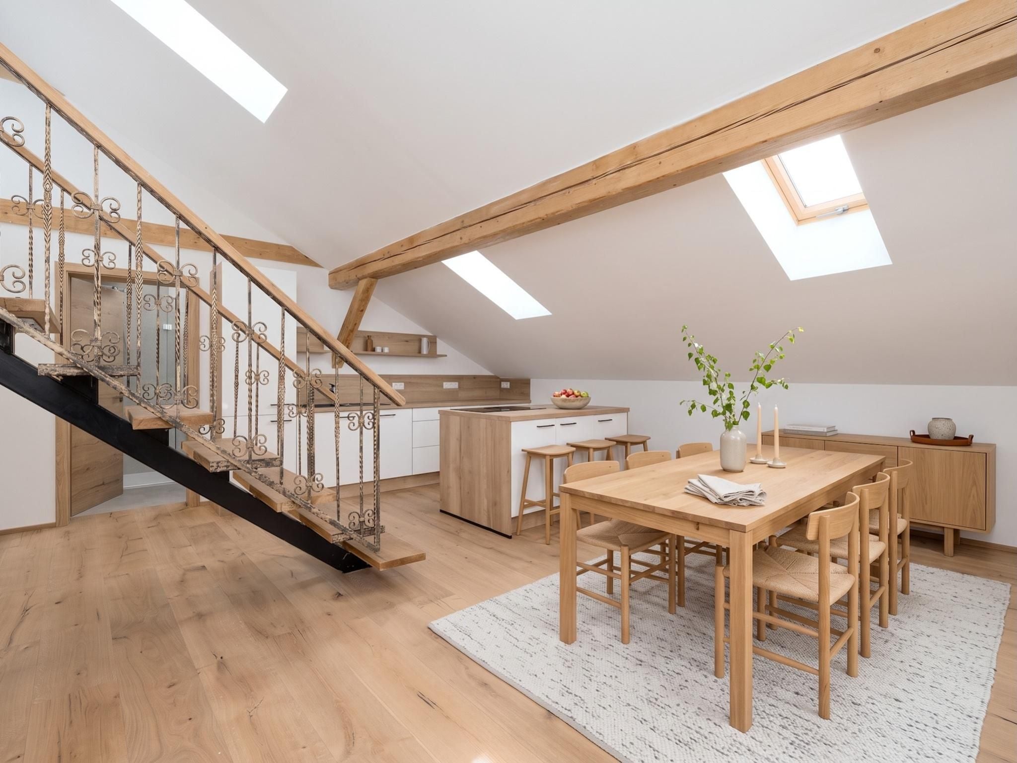 A spacious loft with a wooden staircase, a dining area, and a kitchen.
