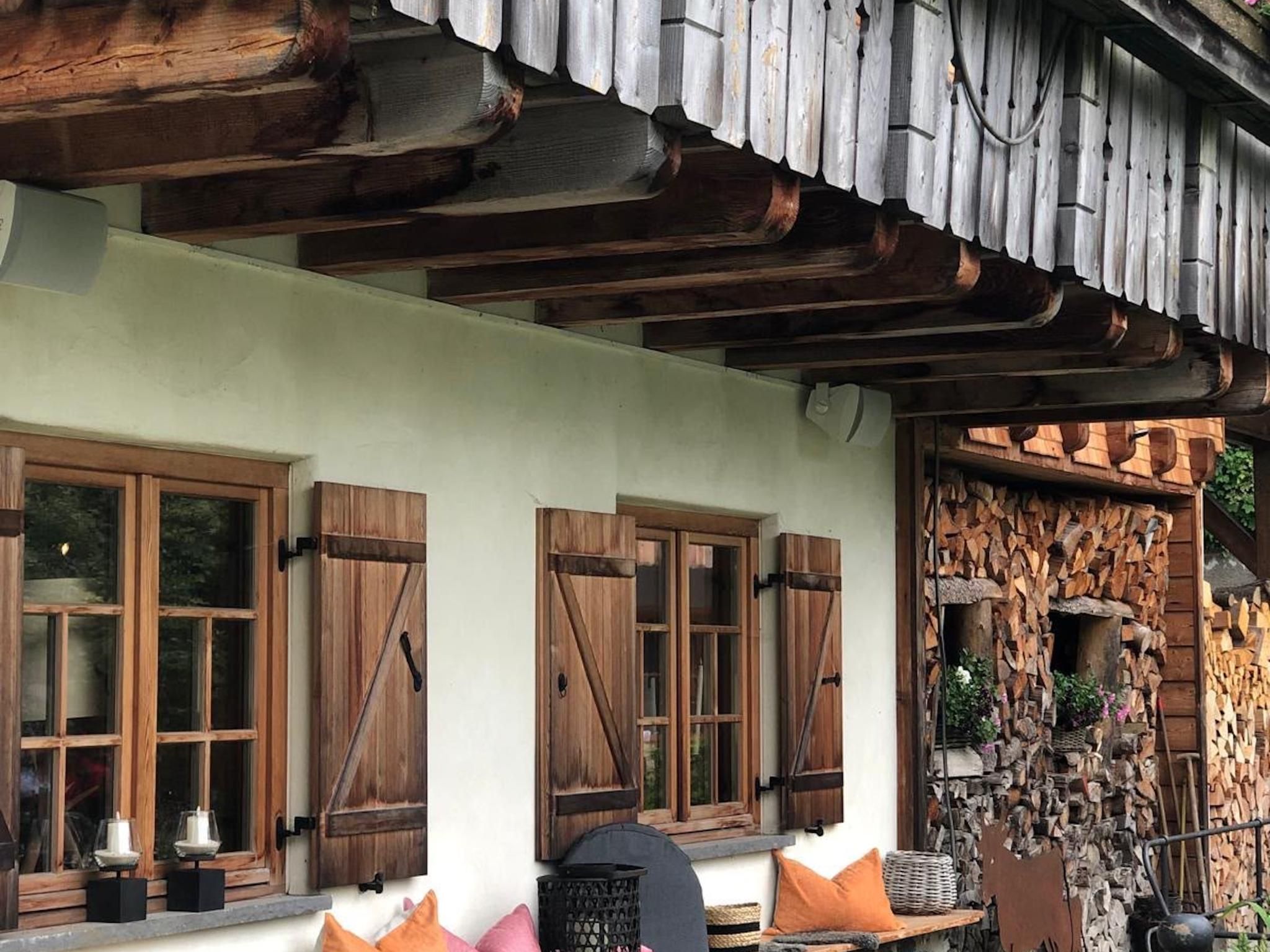 Ein rustikales Gebäude mit Holzläden, einer Steinwand mit Kamin und einer Bank mit Kissen.