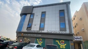 Un immeuble à plusieurs étages dont le rez-de-chaussée est occupé par des commerces et qui affiche une enseigne indiquant un service disponible 24 heures sur 24.