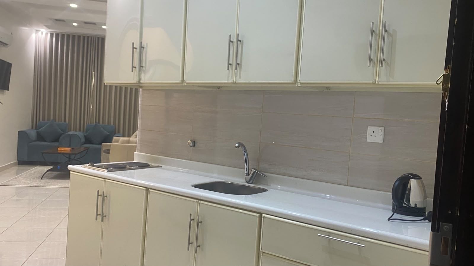 A modern kitchen with a double sink, white cabinets, and a kettle on the countertop.