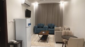 A modern living room with a sofa set, a coffee table, a TV mounted on the wall, and a refrigerator. - AlDurra AlRaqia (Medina)