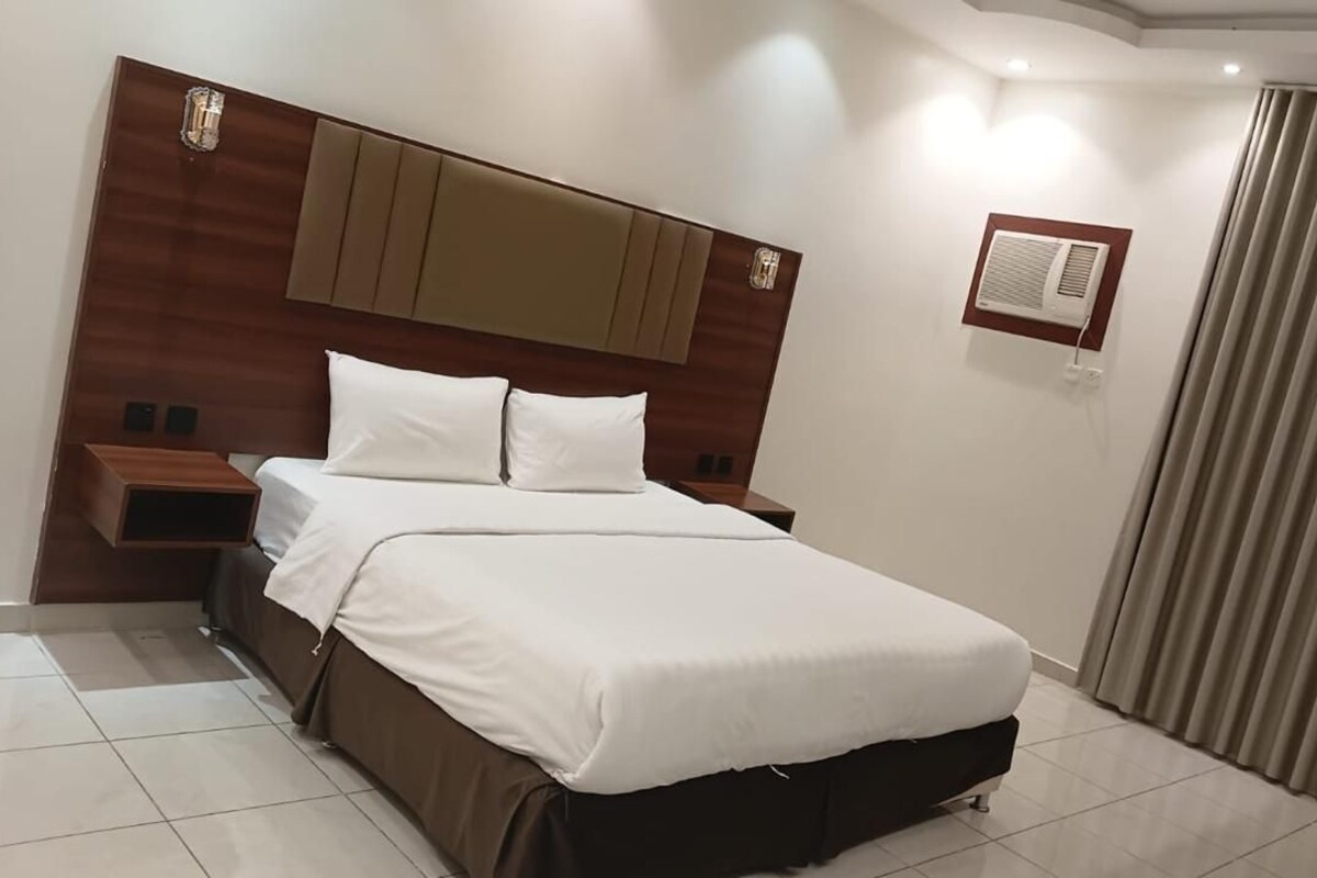 A hotel room with a large bed, a wooden headboard, a bedside table, and a curtain.