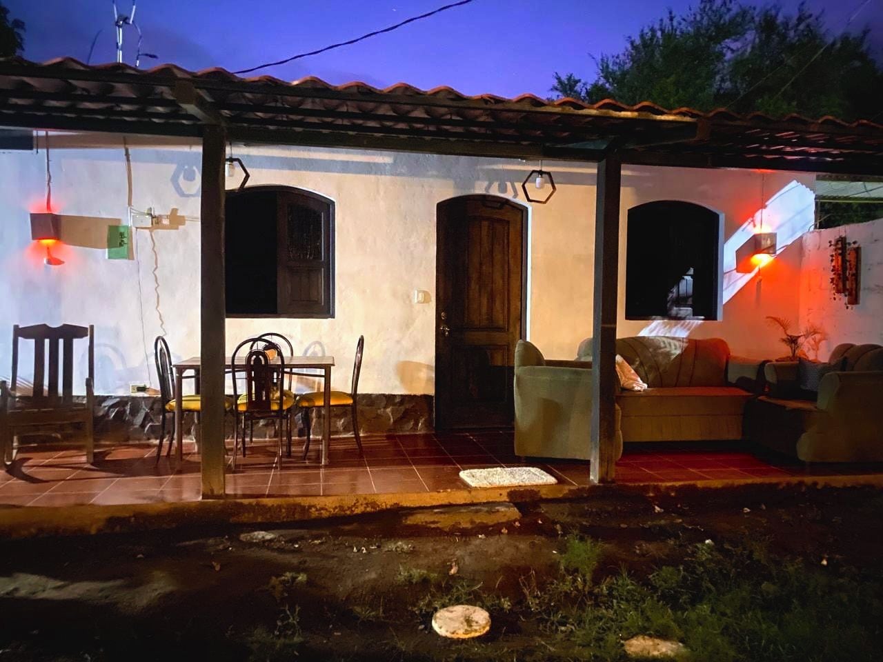 Une maison dotée d’un porche abrité, d’un coin repas avec des chaises et une table, et d’un salon avec un canapé et un téléviseur.