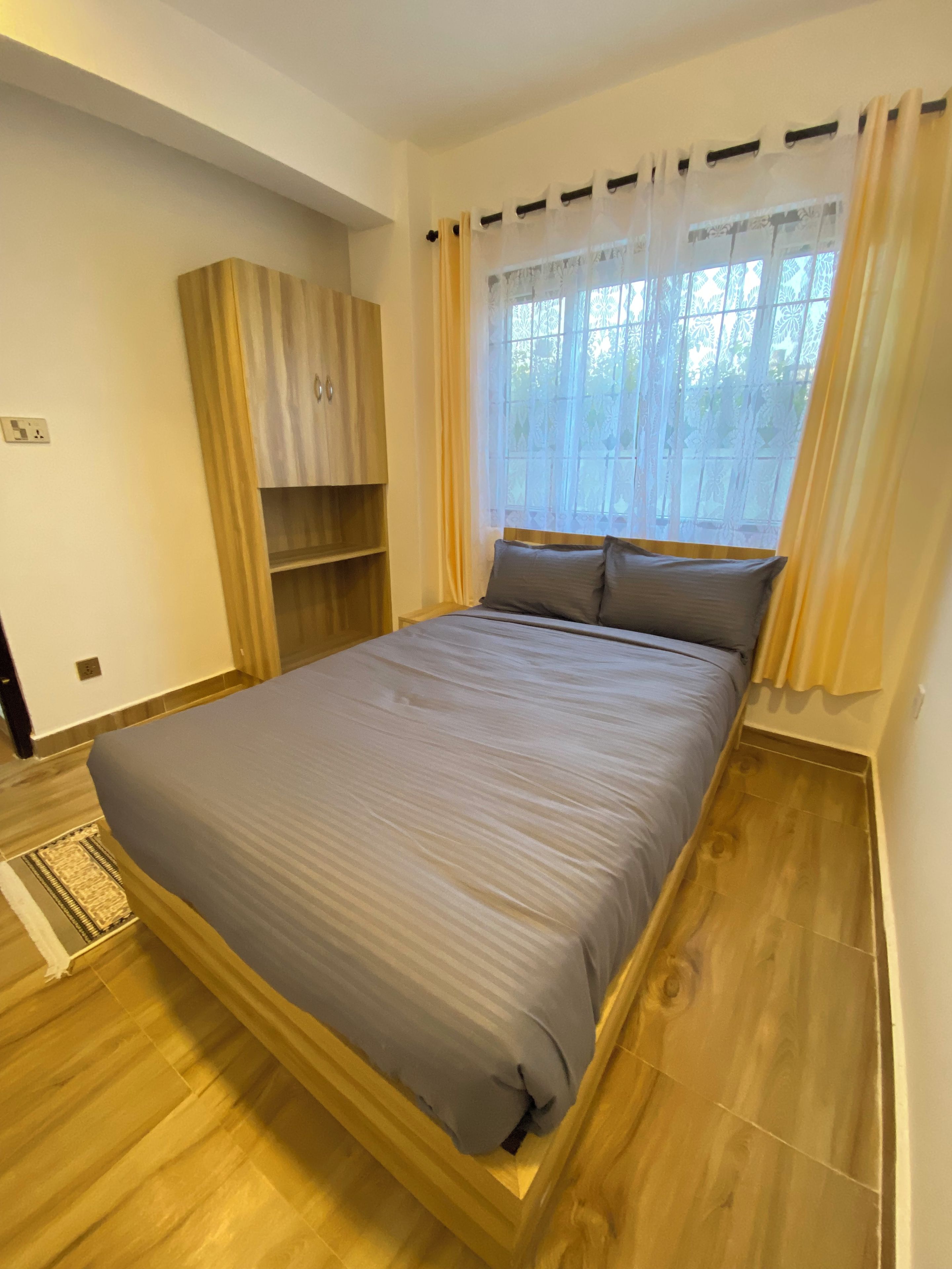 Ein Schlafzimmer mit einem Bett, Holzboden, einem Fenster mit Vorhängen und einem Einbauschrank.