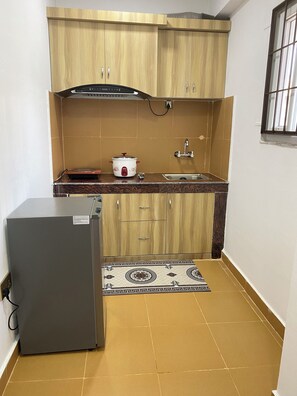 A compact kitchen with wooden cabinets, a built-in stove, a sink, and a refrigerator. - The Silver leaf  (Budhanilkanth)
