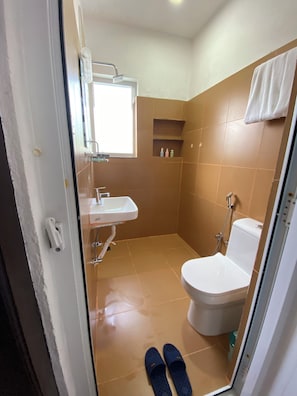 A bathroom with a toilet, sink, and shower. There are slippers on the floor. - The Silver leaf  (Budhanilkanth)