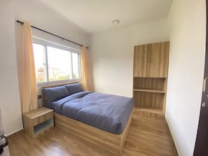A bedroom with a bed, a window, a wooden wardrobe, and a small wooden table. - The Silver leaf  (Budhanilkanth)