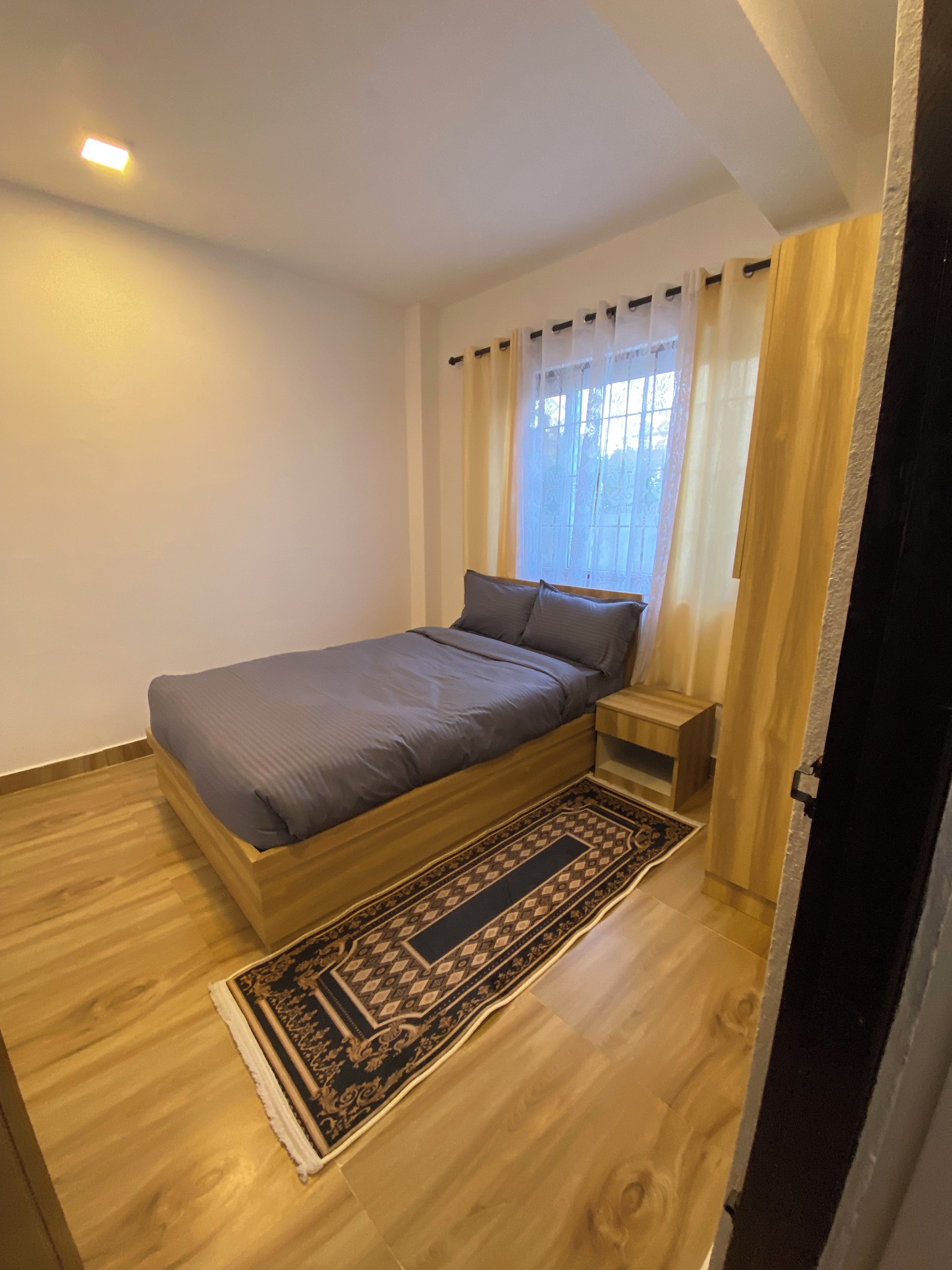 Un dormitorio con una cama individual, una mesita de noche, piso de madera y una alfombra estampada.