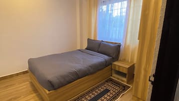 Un dormitorio con una cama individual, una mesita de noche, piso de madera y una alfombra estampada.