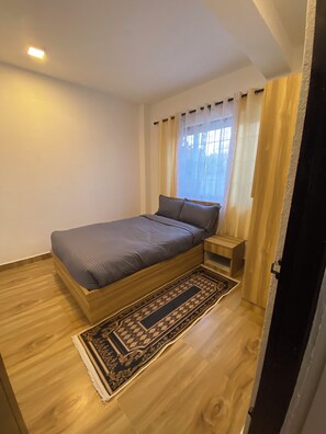 A bedroom with a single bed, a nightstand, a wooden floor, and a patterned rug. - The Silver leaf  (Budhanilkanth)