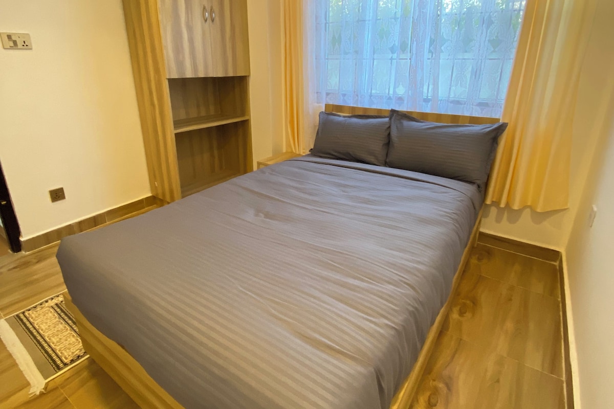 A bedroom with a bed, wooden flooring, a window with curtains, and a built-in wardrobe.