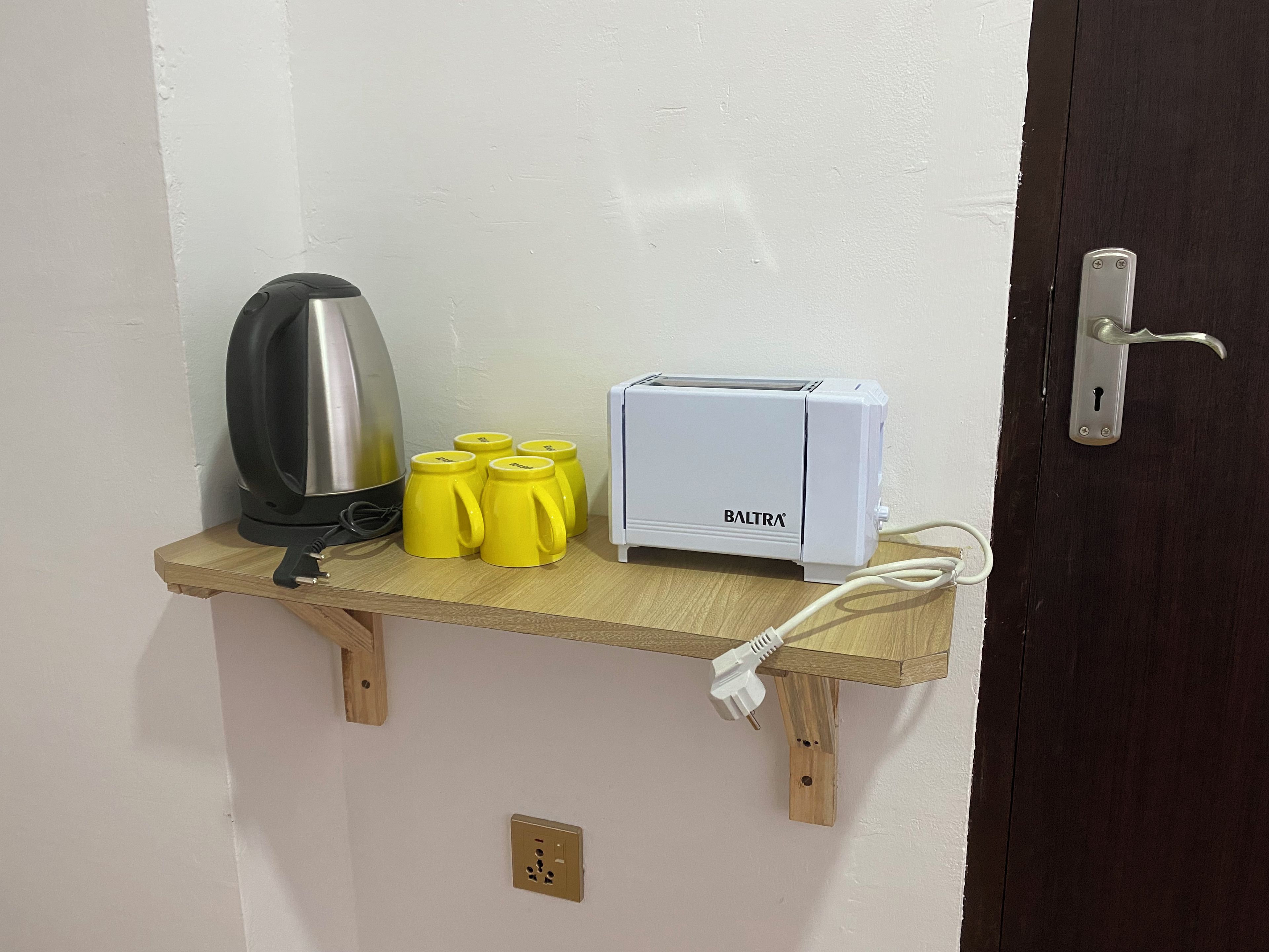 A small wooden shelf with a kettle, a toaster, and four yellow mugs.