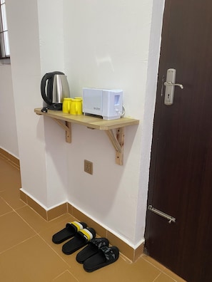 A small wooden shelf with a kettle, a toaster, and yellow cups against a white wall. - The Silver leaf  (Budhanilkanth)