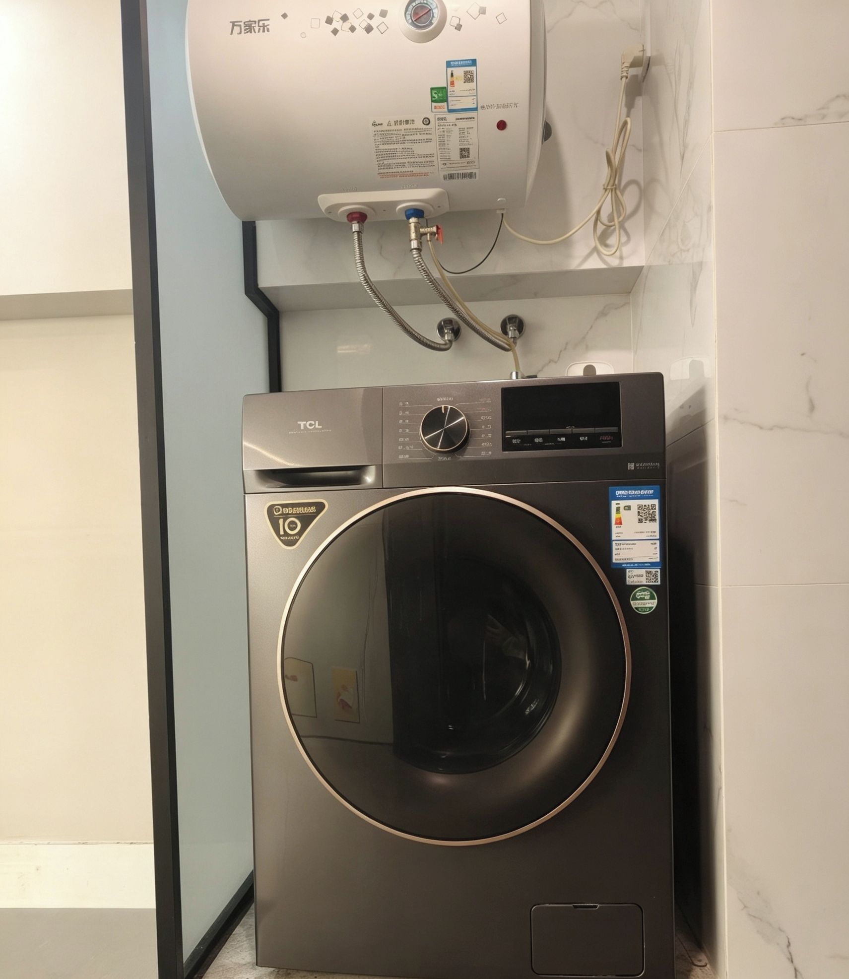 A front-loading washing machine with a control panel, a water heater above it, and a marble-tiled wall.