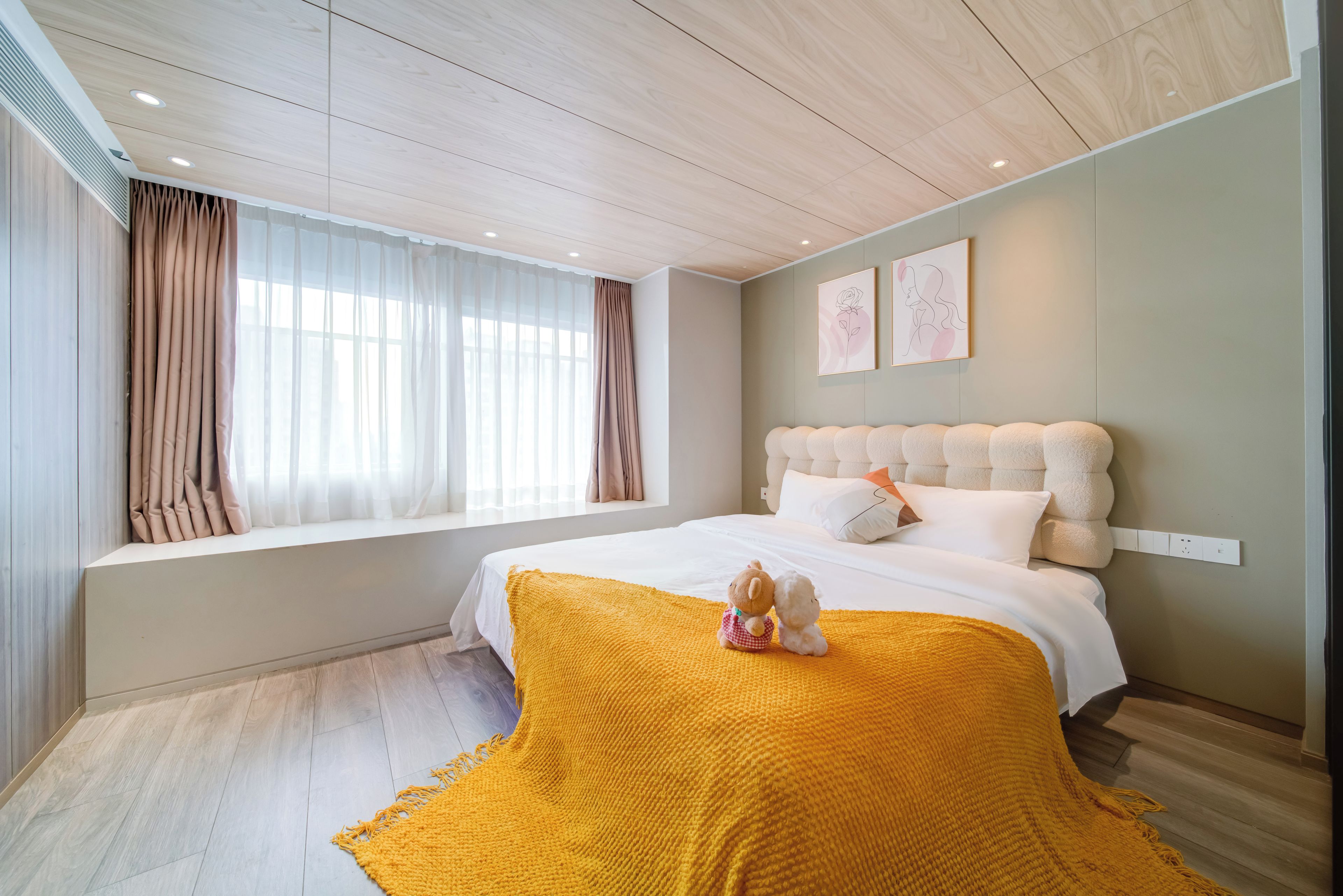 A bedroom with a large window, a bed with a yellow throw, and a headboard with a tufted design.