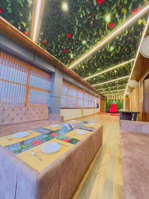 A restaurant with a long communal table, cushioned seating, and a green leafy ceiling. - Hotel Diamond Palace, Bhopal (Bhopal)