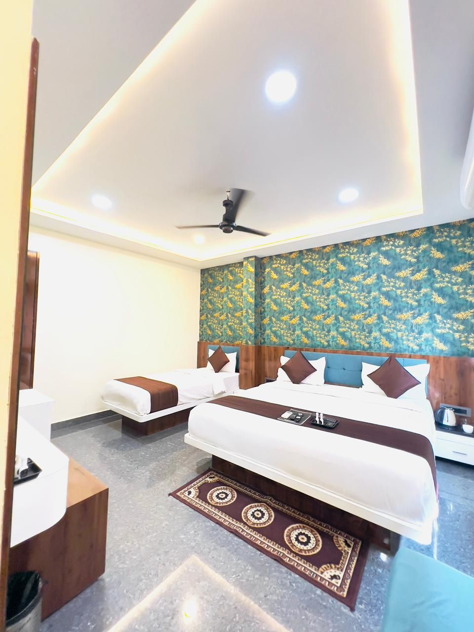 Una habitación de hotel con cama, mesitas de noche, ventilador de techo y alfombra estampada.