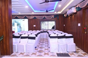 Un salón de conferencias con hileras de sillas, un ventilador de techo y un equipo de aire acondicionado.