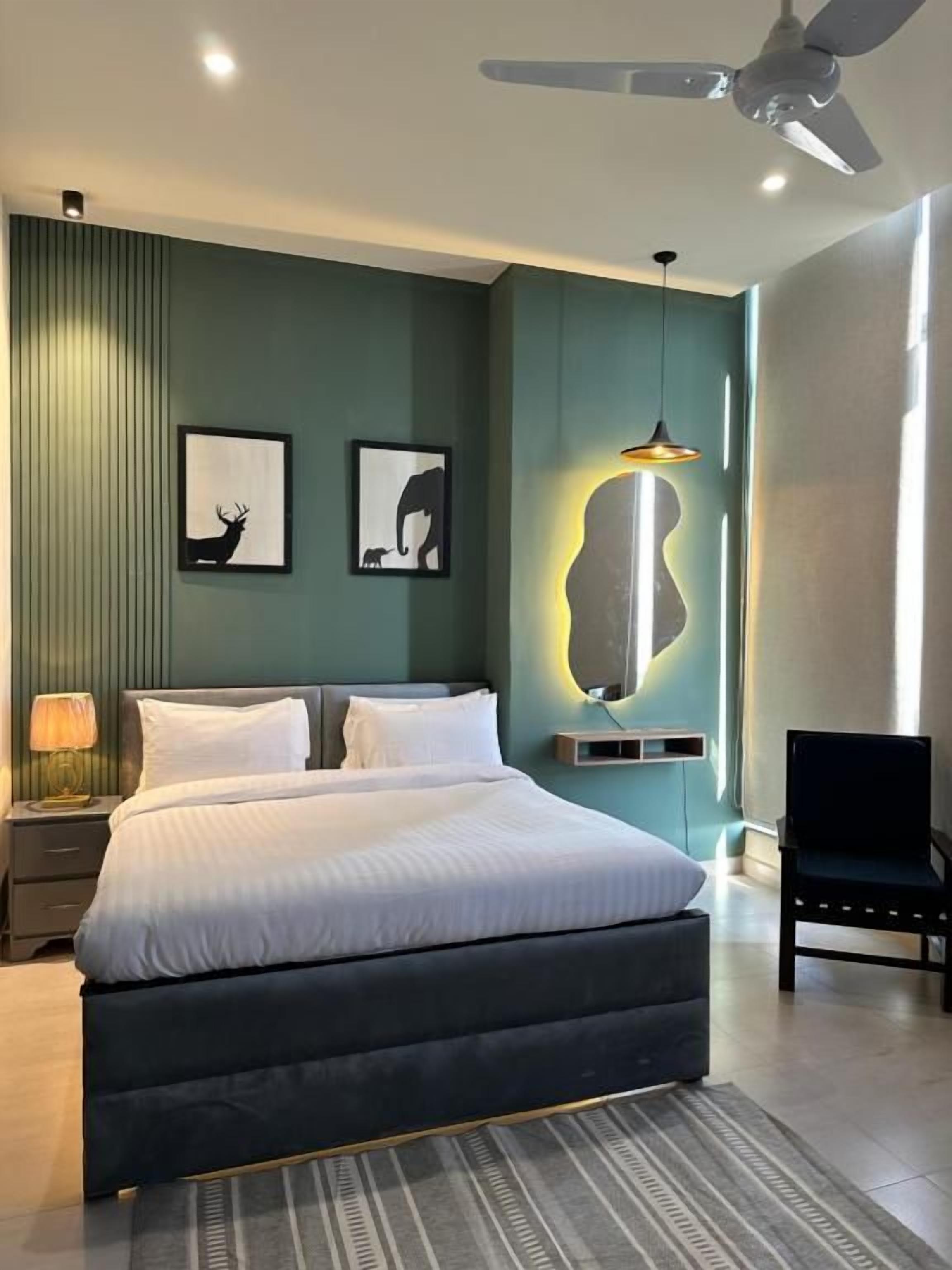 A modern bedroom with a large bed, a ceiling fan, wall-mounted artwork, and a bedside table with a lamp.