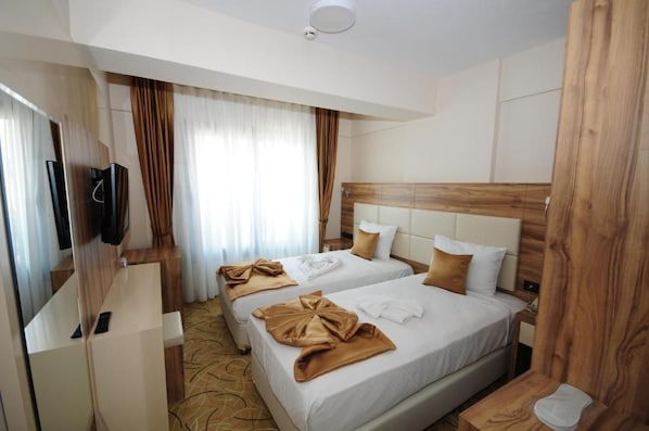 Habitació d'hotel amb dos llits, una televisió, un panell de capçalera de fusta i una finestra amb cortines.