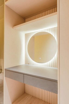 A modern vanity with a round mirror and built-in lighting, a grey countertop, and a wooden slat design on the lower half. - The Avenue Galle (Wanchawala)