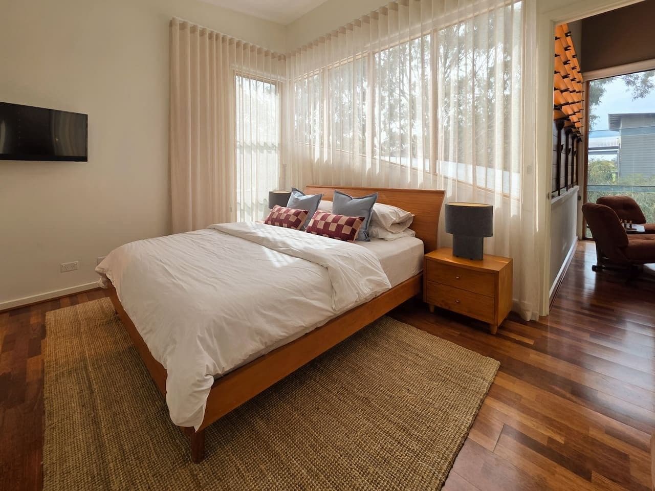 Une chambre moderne avec un lit en bois, une literie blanche et une grande fenêtre ornée de rideaux légers.
