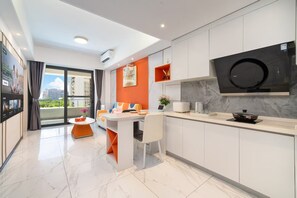 Una cocina moderna con horno empotrado, un comedor con mesa blanca y detalles en naranja, y un amplio ventanal con vistas a la ciudad.
