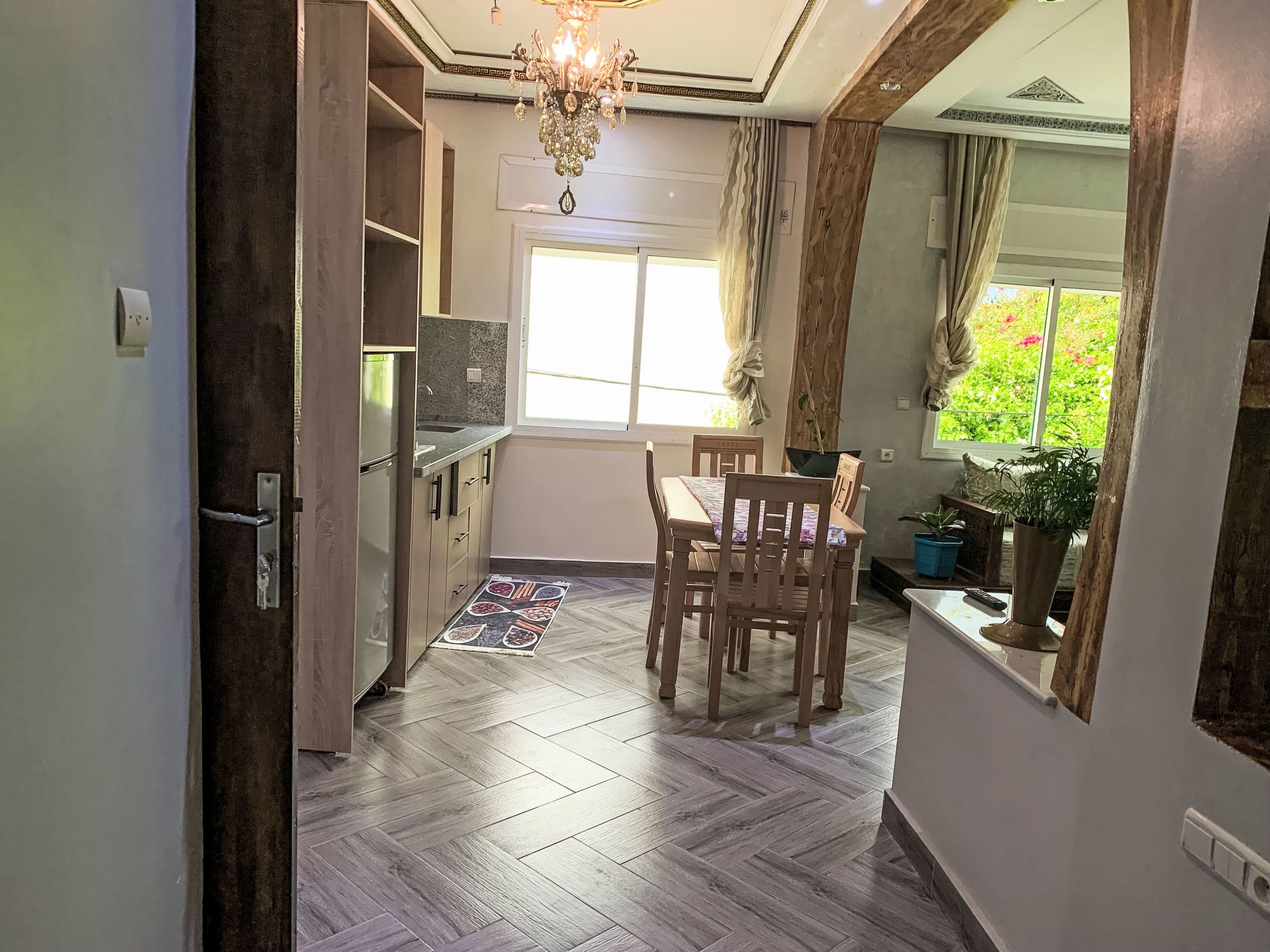 A kitchen with a dining area, wooden flooring, a chandelier, and a window with curtains.