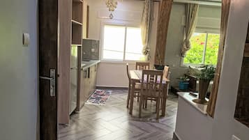 A kitchen with a dining area, wooden flooring, a chandelier, and a window with curtains.