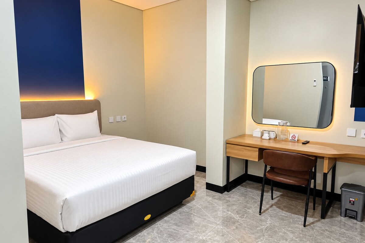 A hotel room with a bed, a desk, a chair, and a mirror.
