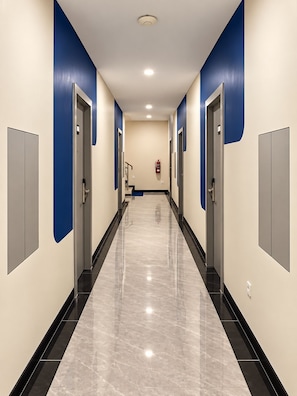A corridor with doors on both sides, a fire extinguisher mounted on the wall, and a ceiling light. - Center Inn Solo Baru (Grogol)
