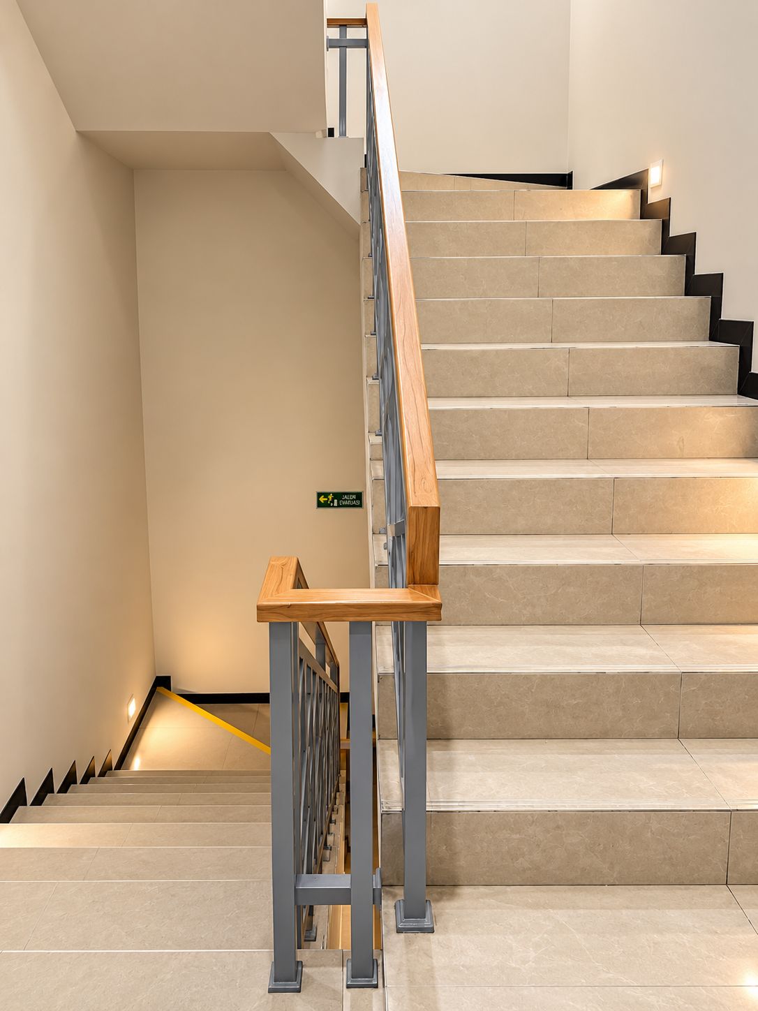 A modern staircase with a wooden handrail and metal balusters, leading to a landing with a sign.