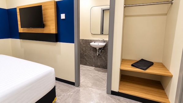 A hotel room with a bed, a TV mounted on the wall, a bathroom with a sink, and a shelf with a towel. - Center Inn Solo Baru (Grogol)