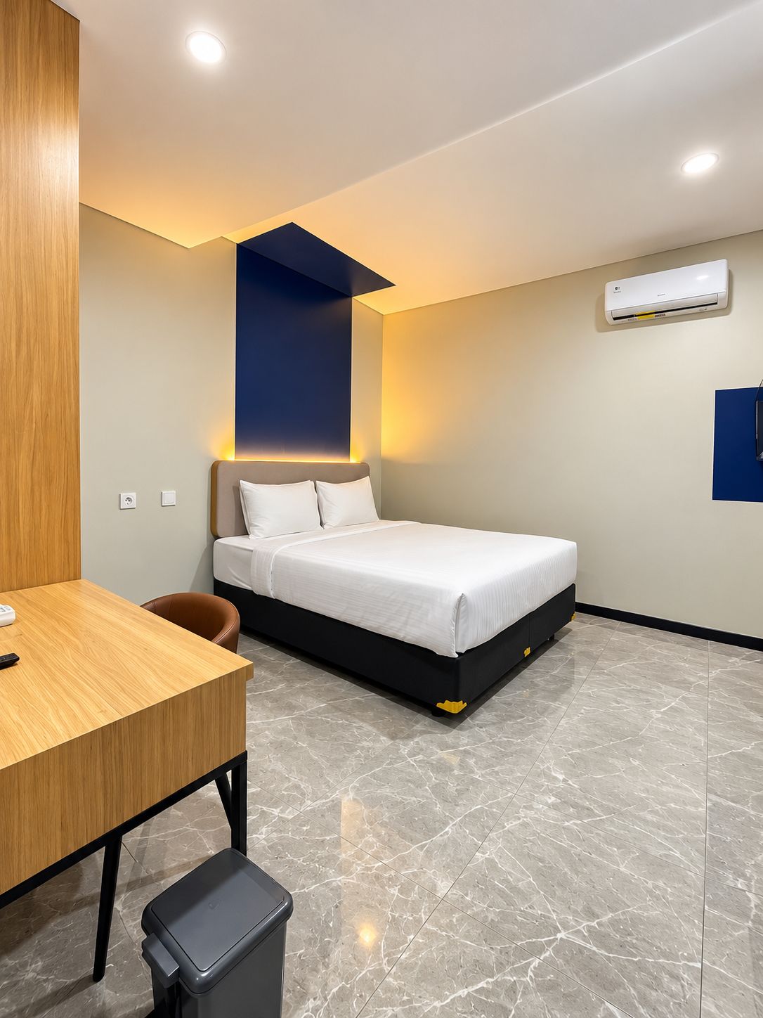 A modern hotel room with a bed, a desk, and a trash bin.