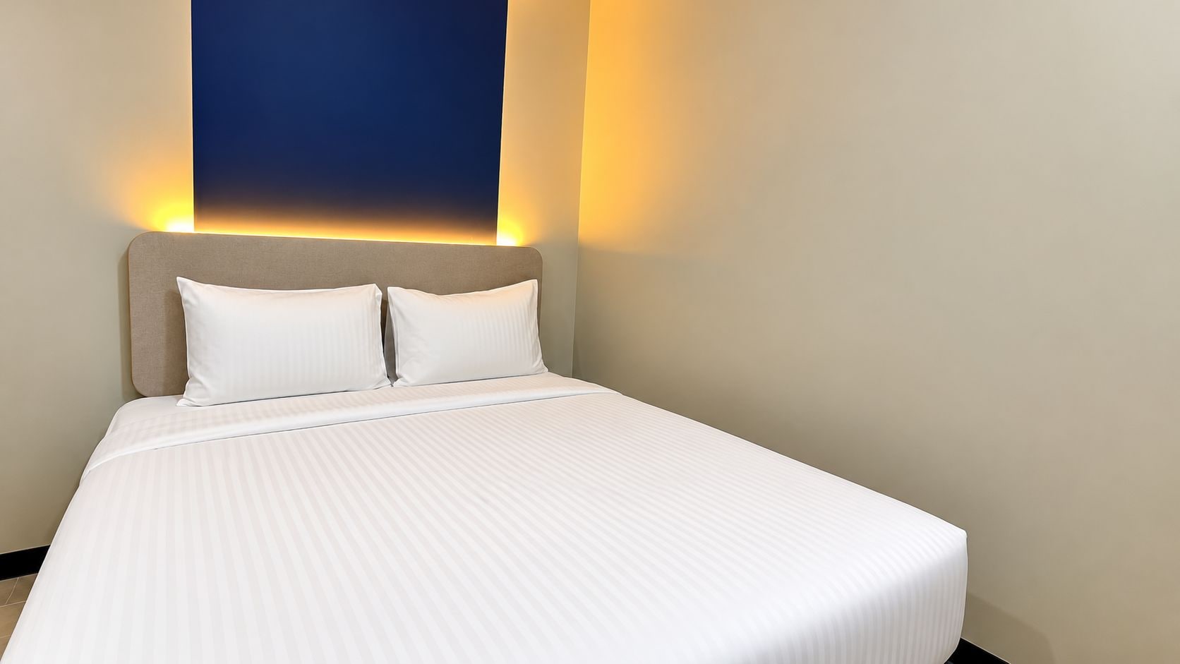 A hotel room with a bed, two pillows, and a headboard.