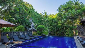 A swimming pool with a stone wall, surrounded by lush greenery and a statue.